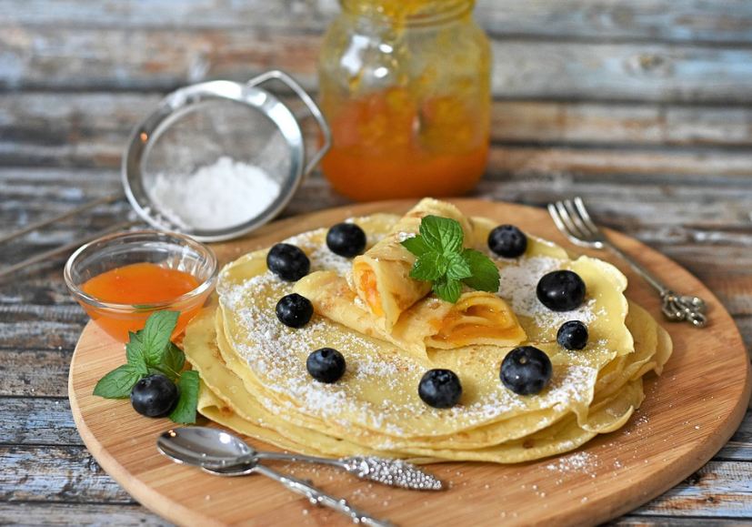 pancakes with sugar powder, mint leaves, and blackberries on a plate