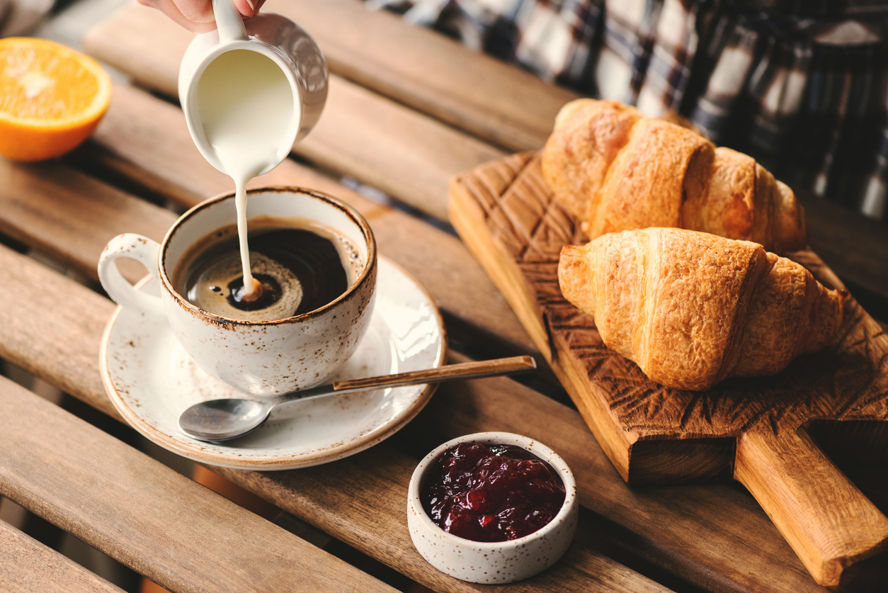 a breakfast table with croissants, jam and coffee, with cream being poured out on it