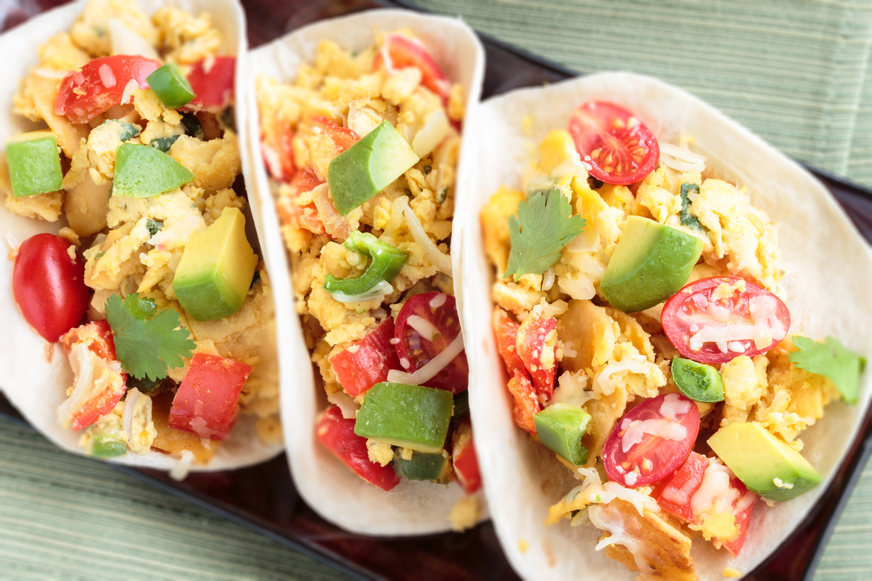 Tacos filled with migas, a Tex-Mex dish of eggs scrambled with red bell pepper, onions, jalapenos, cheese, topped with avocado, cilantro, cherry tomatoes