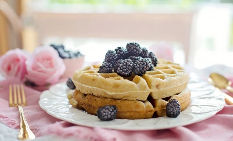 a picture of waffles on a white plate. There are berries on the waffles. A fork and spoon is placed besides the plate