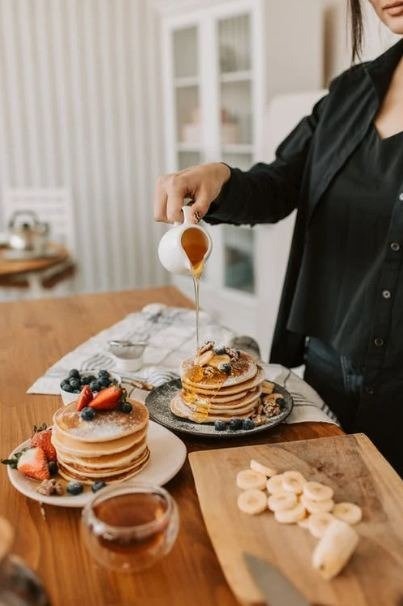 A person pouring maple syrup on pancakes.
