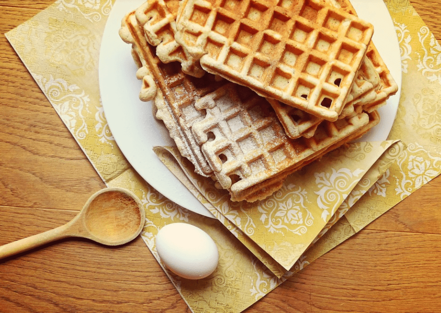 waffle stack with powdered sugar, plate, table cloth, egg, wooden spoon