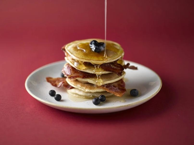 stacks of pancake with blueberry, bacon, and syrup
